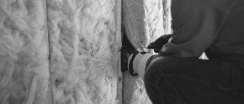 Close up of a worker installing fibre insulation into the wall of a building. Photo by Erik Mclean on Unsplash.