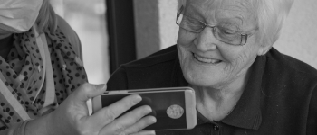 A senior woman smiling at a smartphone that's being held for her to look at. Photo by Georg Arthur Pflueger on Unsplash.
