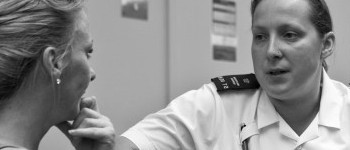 A female prison officer in uniform is speaking to a woman with her back to us.